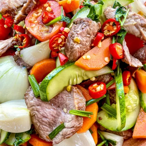 Yum neua, Thai spicy beef salad with tender beef, fresh vegetables, and red chili flakes for a bold, vibrant look.