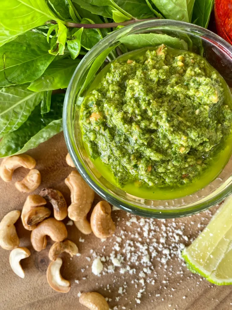 Asian basil pesto in a glass cup with basil leaves, cashews, salt, and a lime wedge.