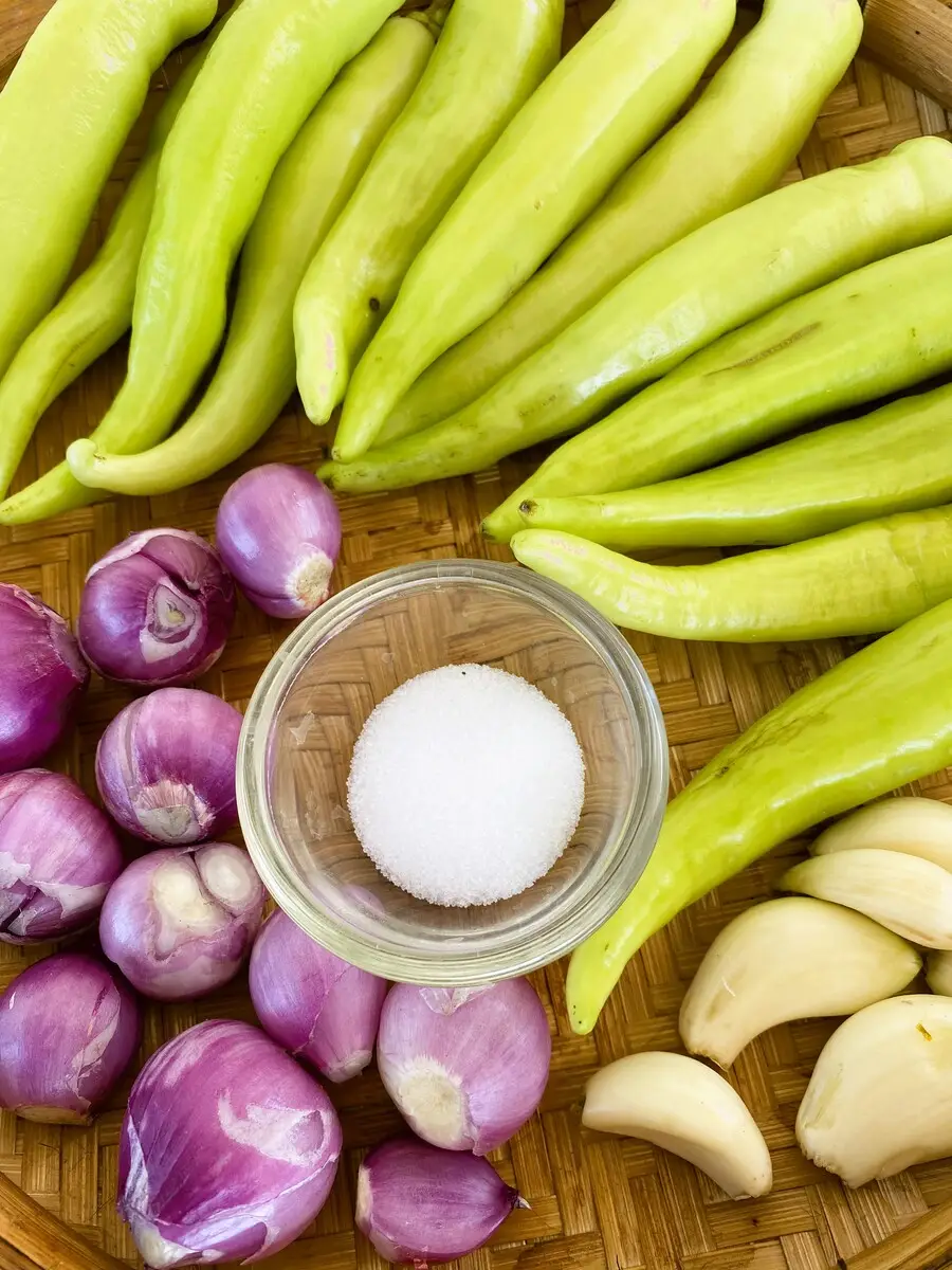 Overhead view of large green chilies, garlic, shallots, and salt in a glass cup.