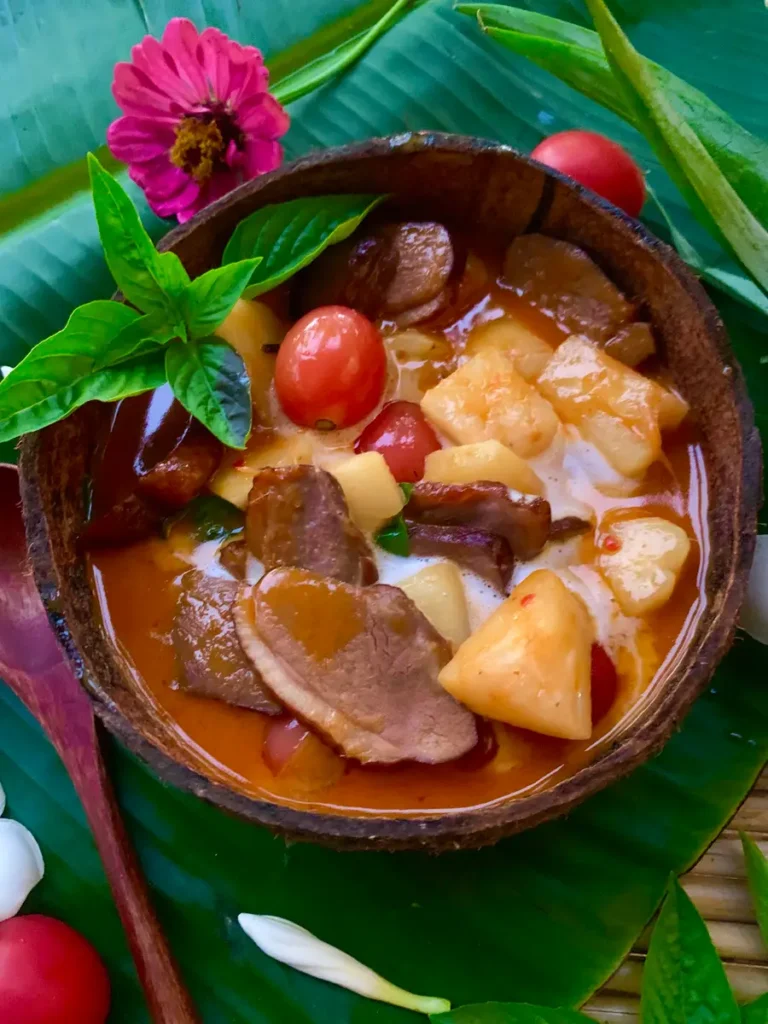 Thai roasted duck curry, gaeng phed ped yang, with pineapple and tomatoes in a coconut shell.
