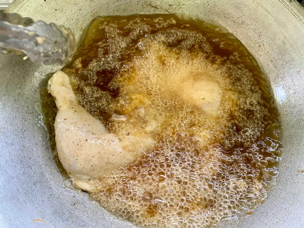Bird's eye view of deep-frying chicken in a deep frying pan.