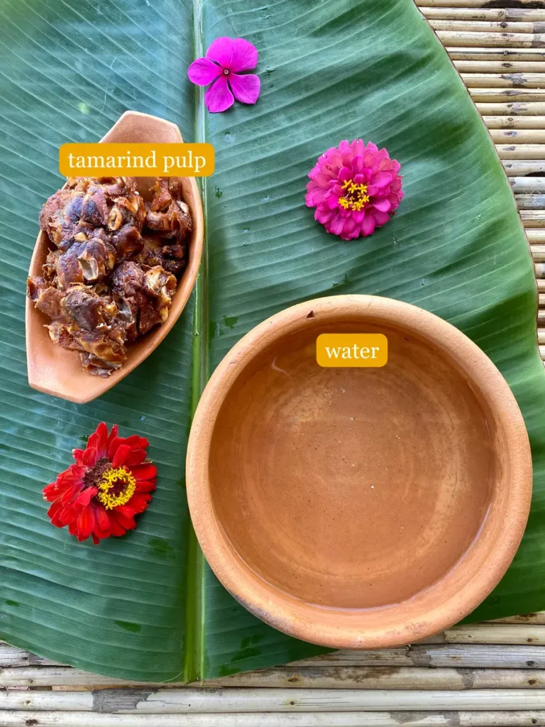 Tamarind pulp and water in clay dishes set on a banana leaf with flowers.