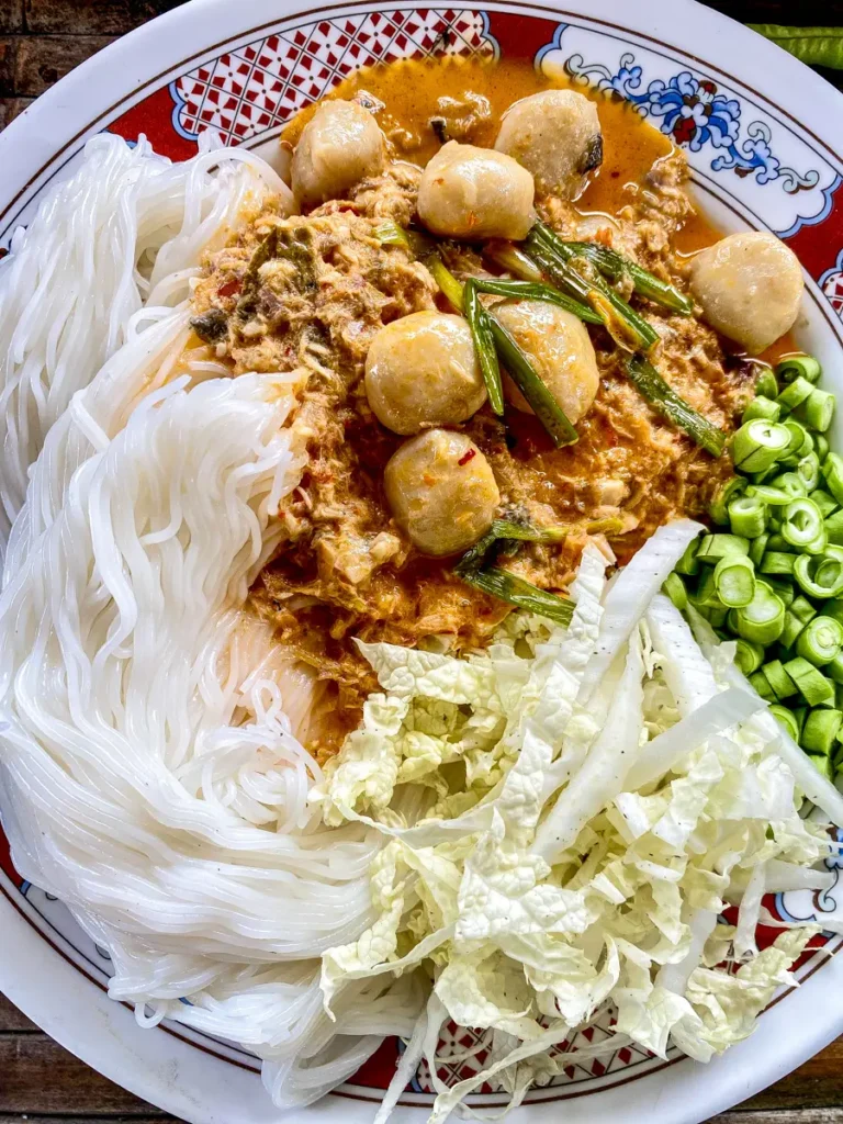 Top-down view of kanom jeen nam ya, served in a white dish with a side of cabbage and chopped yard long beans.