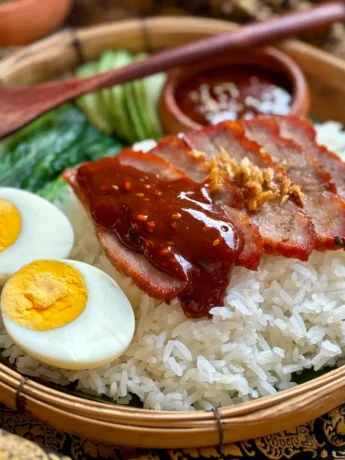 Khao moo dang, Thai red pork, over jasmine rice with cucumber and boiled egg garnish.