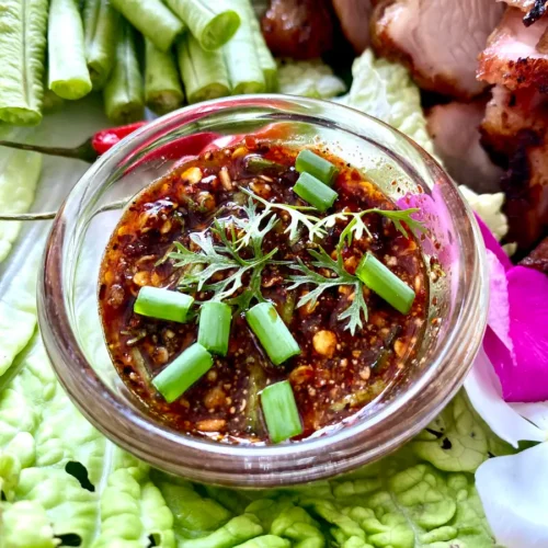 Nam jim jaew dipping sauce with grilled meats and fresh vegetables.