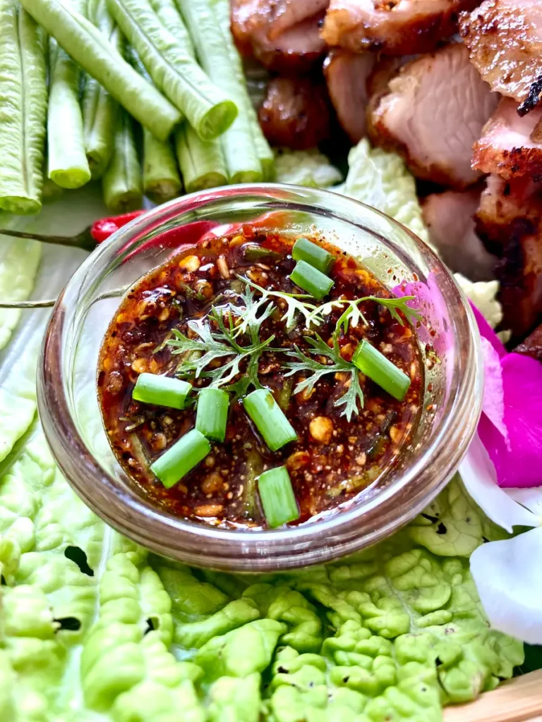 Nam jim jaew dipping sauce with grilled meats and fresh vegetables.