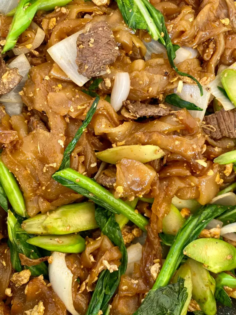 Close-up of stir-fried rice noodles with beef, onions, Chinese broccoli, and garlic.
