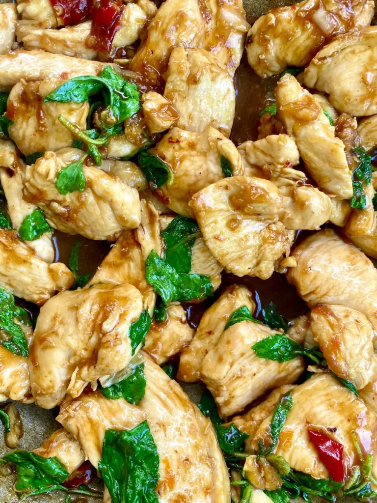 Close-up of stir-fried chicken with Thai holy basil and chilies, coated in a dark brown sauce.