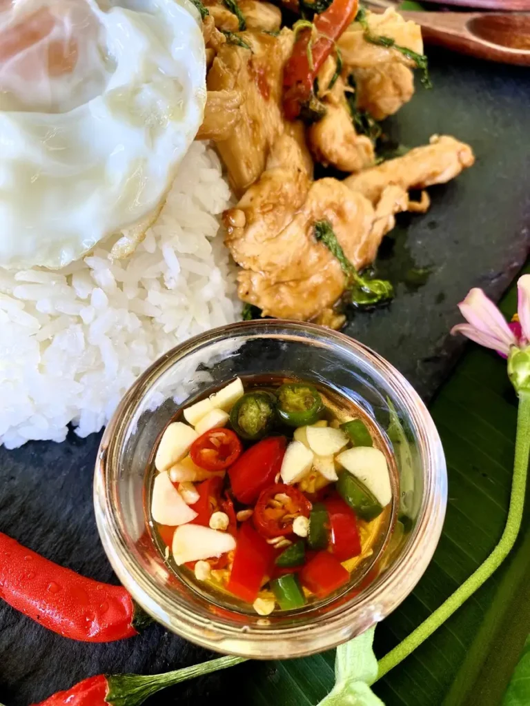 Top-down view of a Thai chili dipping sauce with white rice, a fried egg, and stir-fried basil chicken.