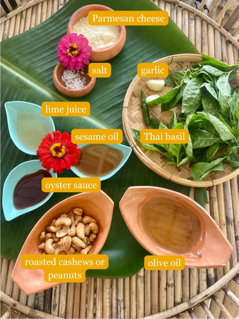 Ingredients for recipe presented on a banana leaf in clay and plastic cups: Parmesan cheese, salt, garlic, Thai basil, lime juice, sesame oil, oyster sauce, roasted cashews, and olive oil.