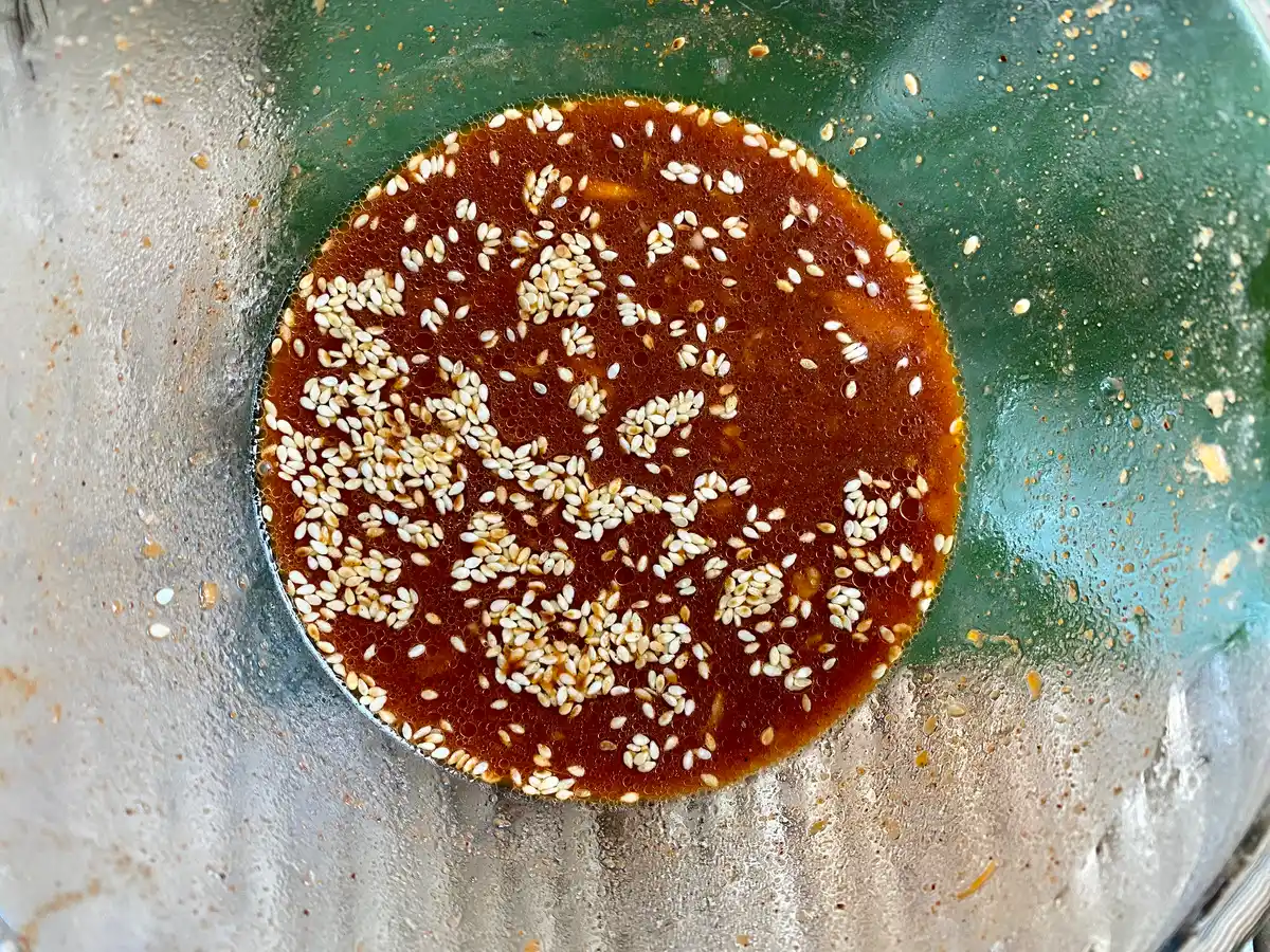 Top-down view of large glass bowl with red sauce and sesame seeds.