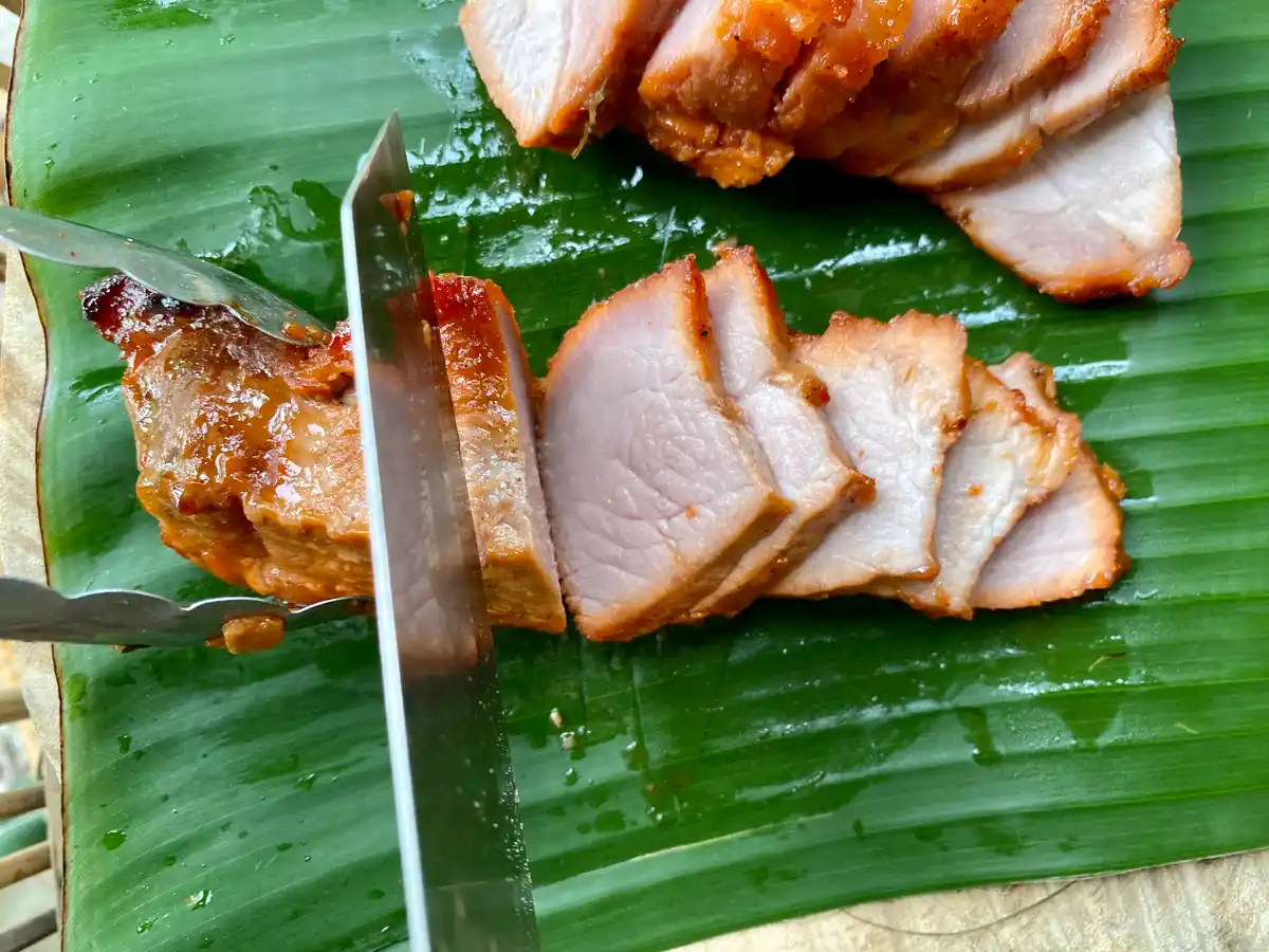 Red pork being sliced on a banana leaf.
