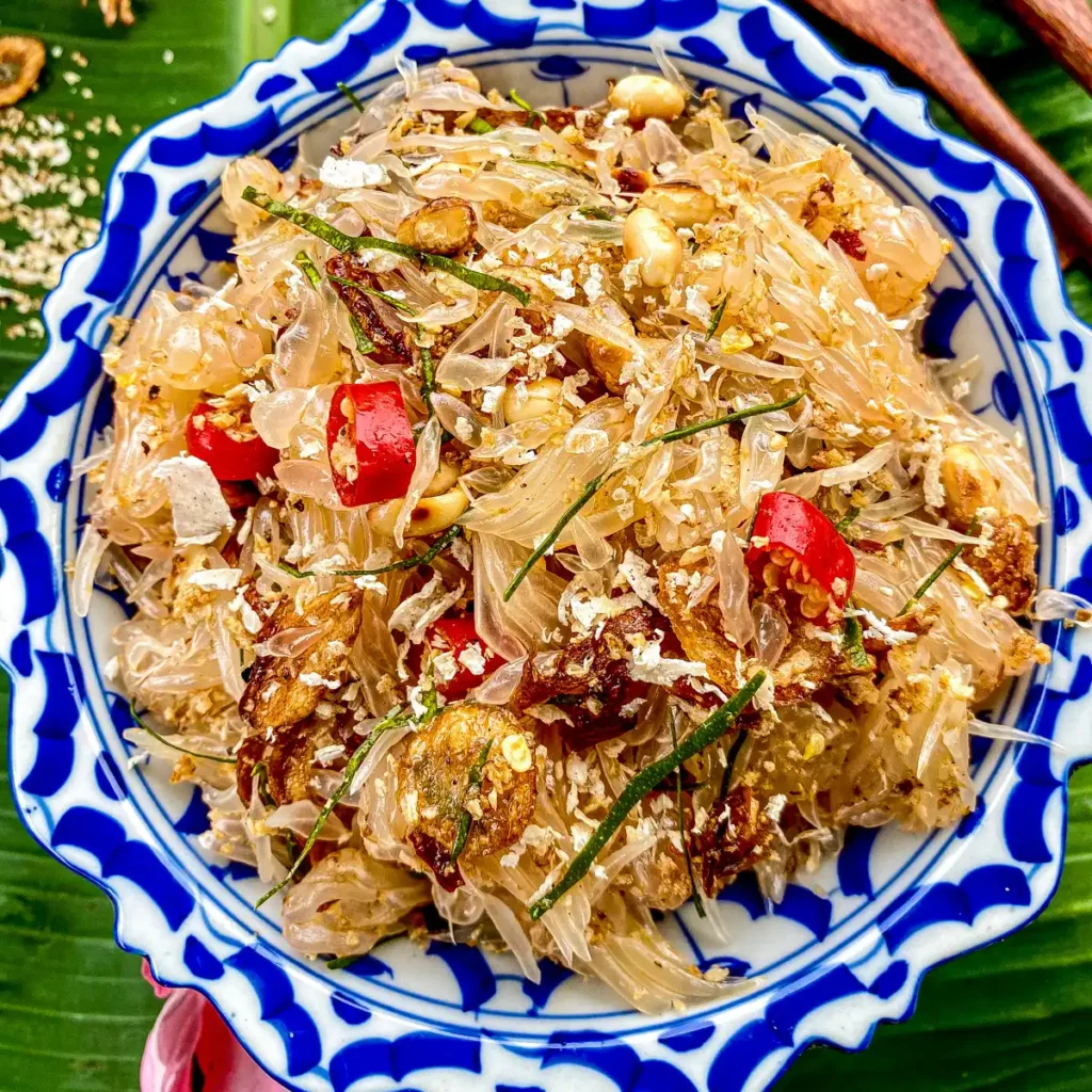 Overhead shot of Thai pomelo salad with shredded pomelo, red chilies, and crispy toppings in traditional patterned bowl.