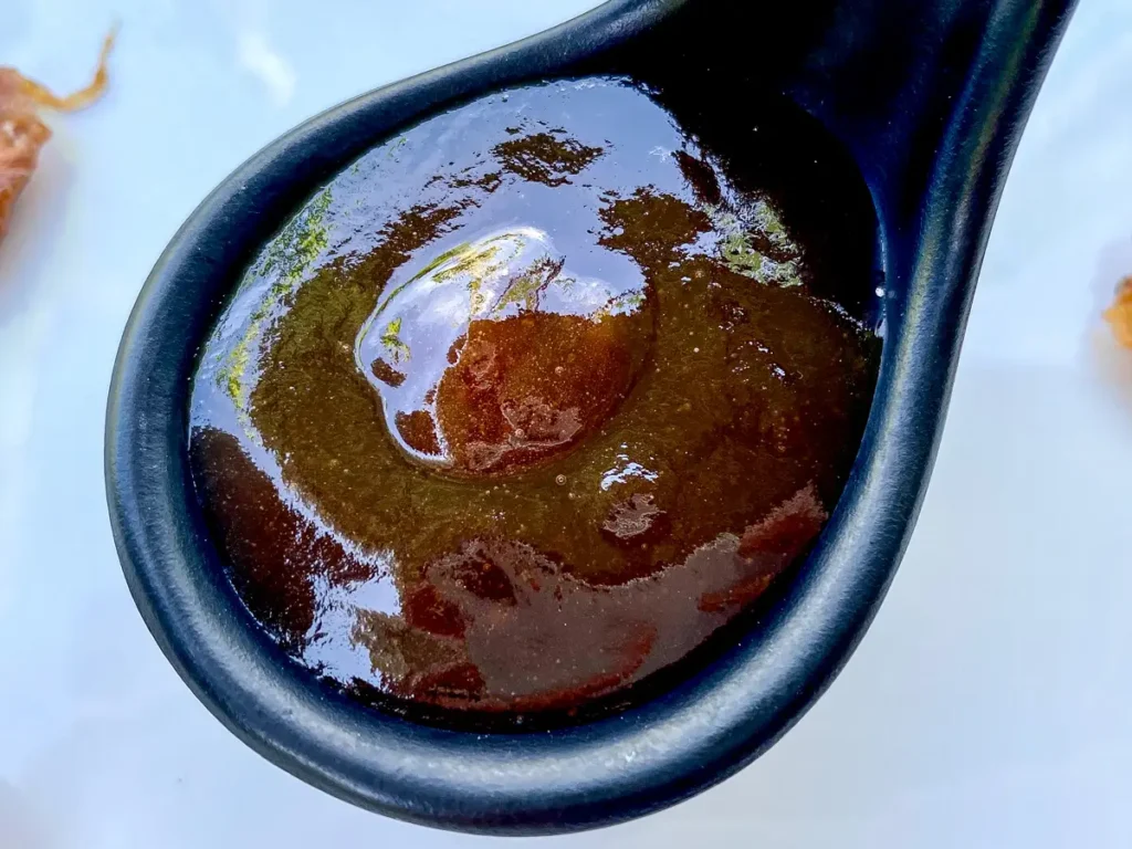 Thai tamarind sauce in a black spoon with sticky, shiny surface.