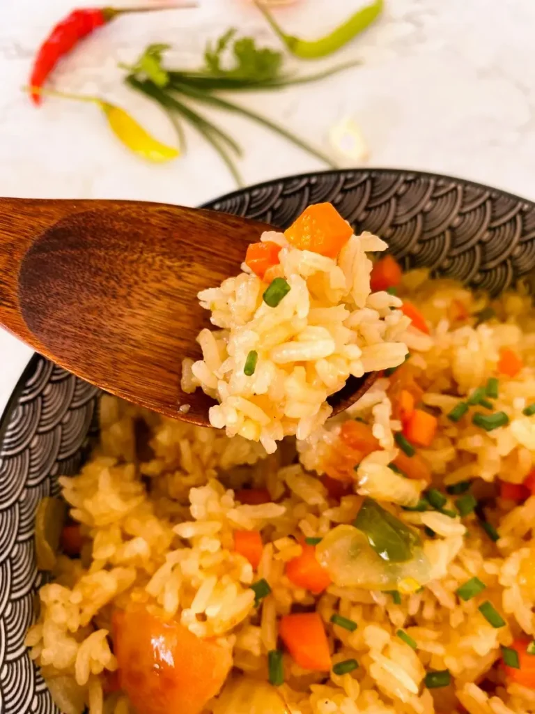 A wooden spoon with a bite of fried rice and vegetables over a blue and white bowl with fried rice with vegetables.