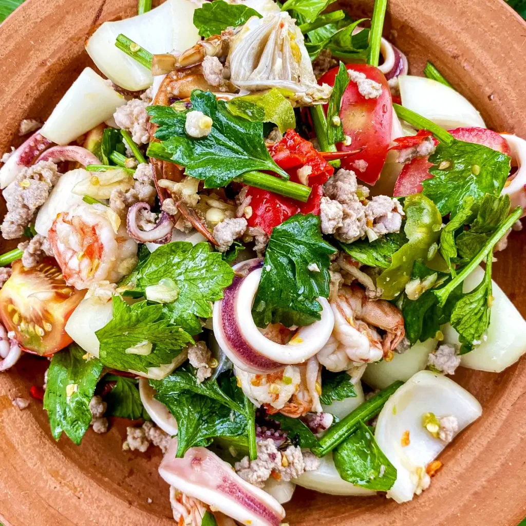Thai yum talay seafood salad with shrimp, squid, minced pork, tomatoes, and celery on a clay plate.