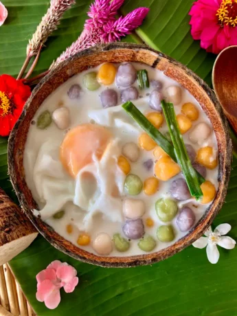 Top-down view of Thai bua loy dessert with glutinous rice balls swimming in coconut milk, served in a coconut shell.
