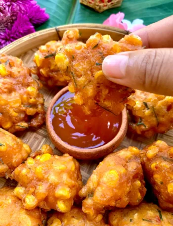 Hand dipping Thai corn fritters into sweet chili sauce.
