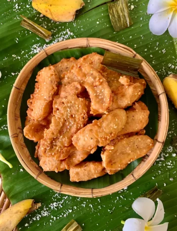 Top-down view of Thai fried bananas on a banana leaf, with flowers and banana peels scattered around.