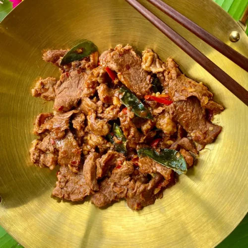 Top-down view of Thai hot and spicy beef stir-fry in a golden dish and wooden chopsticks.