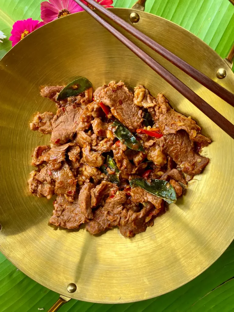 Top-down view of Thai hot and spicy beef stir-fry in a golden dish and wooden chopsticks.