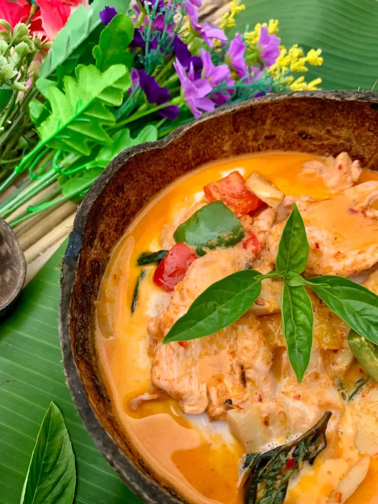 Close-up of Thai red chicken curry served in a coconut shell.