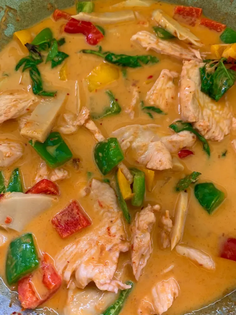 Close-up of Thai red curry with chicken and vegetables like bell peppers and bamboo shoots in a pan.