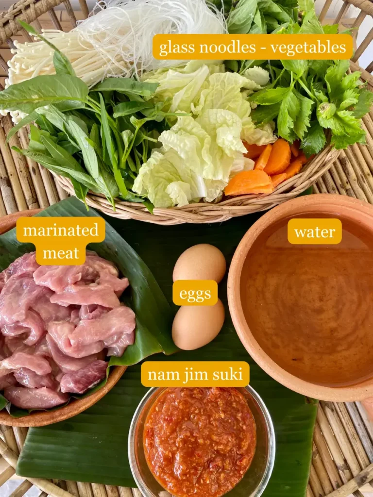 Ingredients for Thai sukiyaki broth; glass noodles, vegetables, marinated meat, eggs, water, and nam jim suki.