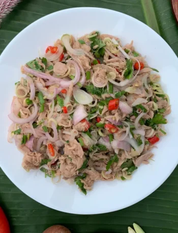 Top-down view of spicy Thai tuna salad with chilies, shallots, lemongrass, and fresh herbs in a white dish.