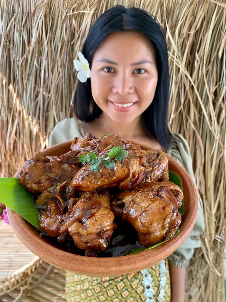Smiling Asian woman presenting clay dish with Coca-Cola chicken wings.