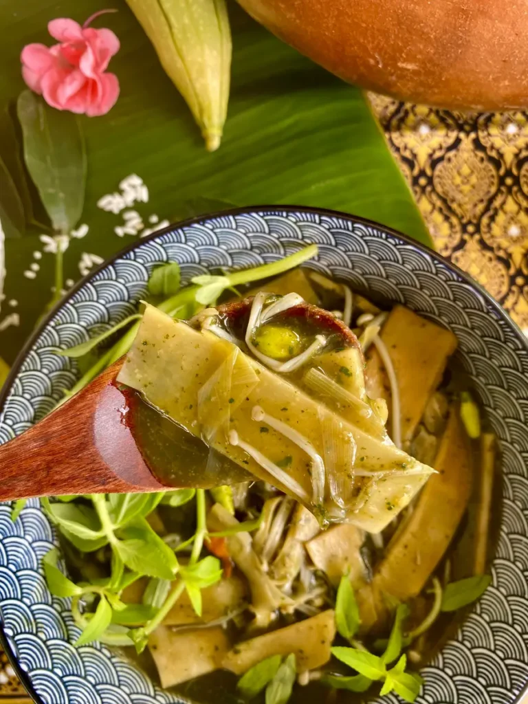 A spoonful of bamboo shoot and soup over a bowl with more bamboo soup.