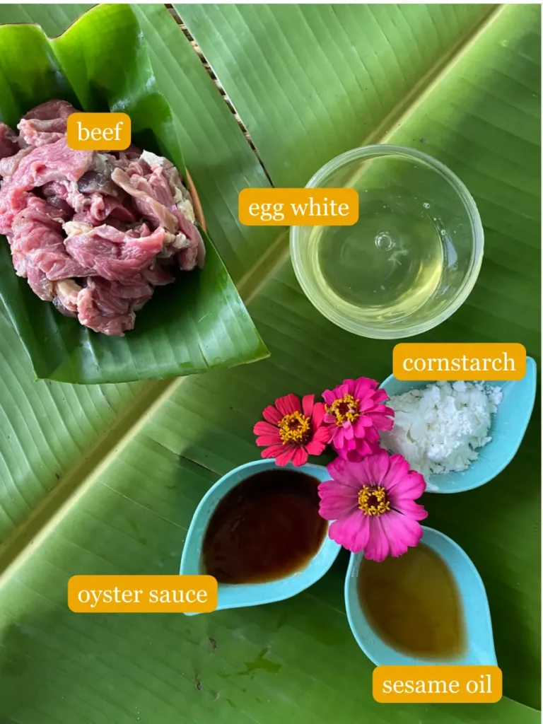 Bird's eye view of ingredients for marinating beef on a banana leaf; beef, egg white, cornstarch, oyster sauce, and sesame oil.