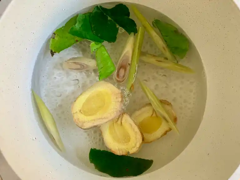 Sliced lemongrass, galangal, and kaffir lime leaves simmering in water to infuse the broth.