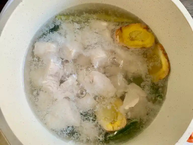 Chicken pieces cooking in aromatic broth with galangal and lemongrass.