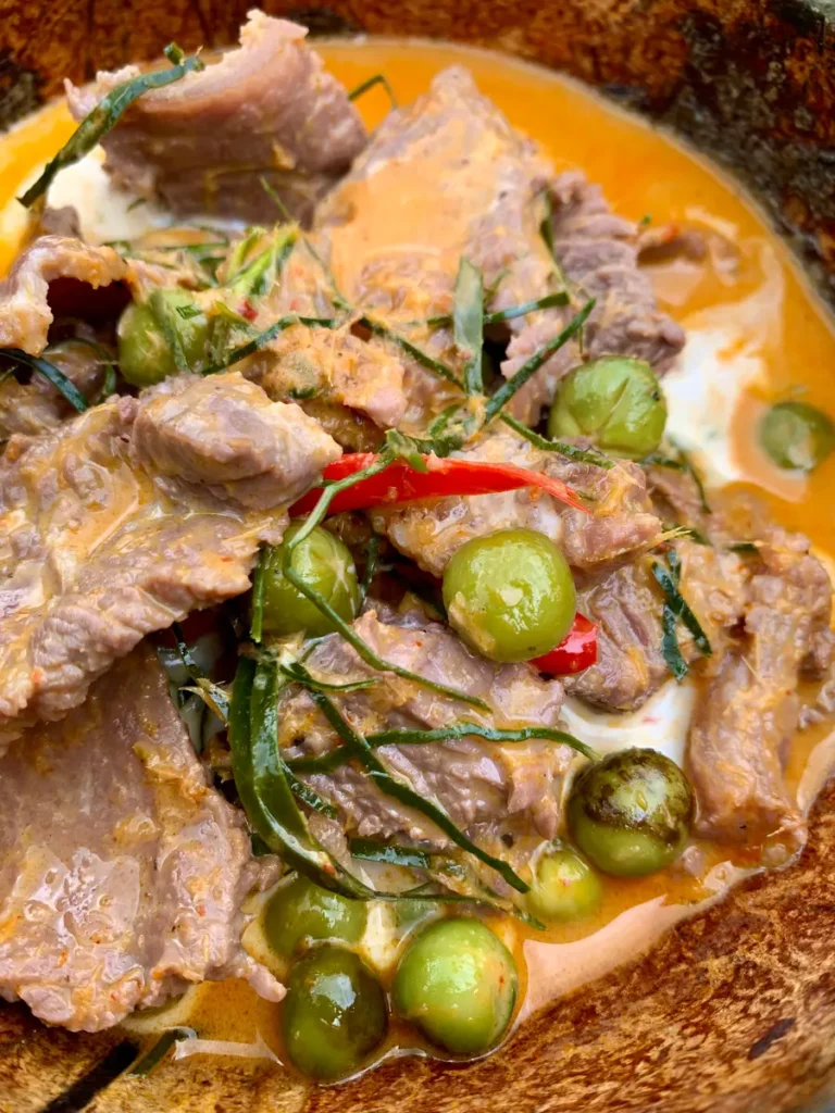 Close-up of coconut milk beef curry with kaffir lime leaves, chilies, and peas.