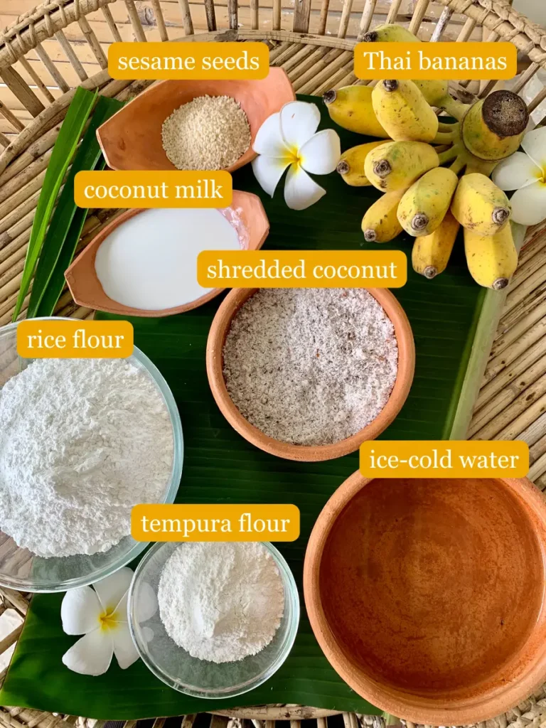 Bird's eye view of fried bananas ingredients; Thai bananas, sesame seeds, coconut milk, shredded coconut, rice flour, tempura flour, and ice-cold water.