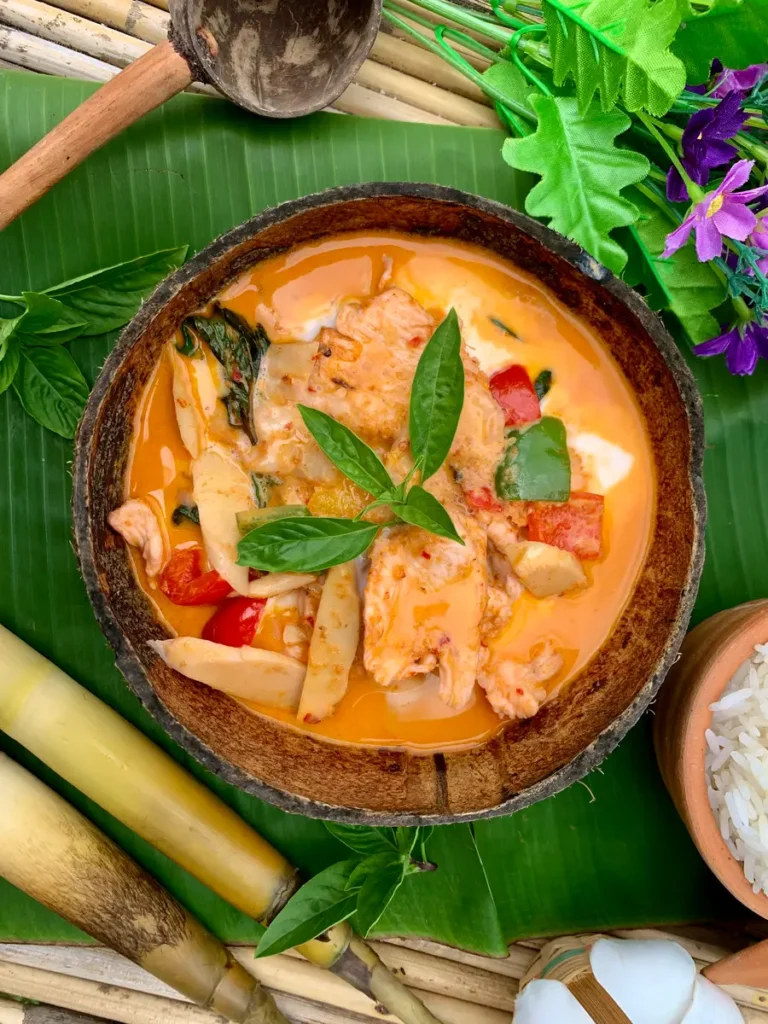 Gaeng daeng curry ; Thai red curry in a coconut shell. Scattered around are fresh bamboo, flowers, basil, and white rice.