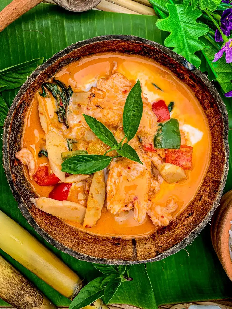 Traditional Thai red curry chicken (gaeng daeng) with rich coconut milk, bamboo shoots, and colorful bell peppers on a banana leaf background.