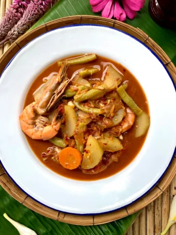 Top-down view of kaeng som, Southern Thai curry with shrimp, carrot and beans in a white dish.