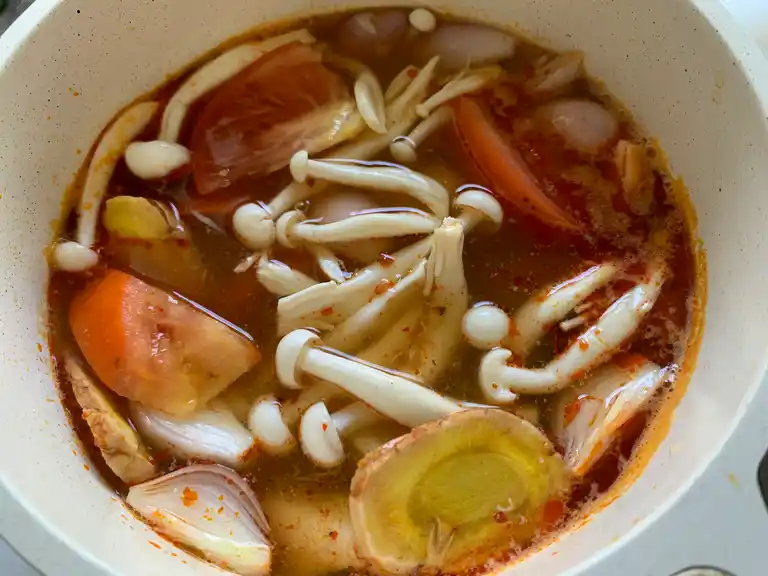 Mushrooms, tomatoes, and shallots simmering in spicy Thai broth.