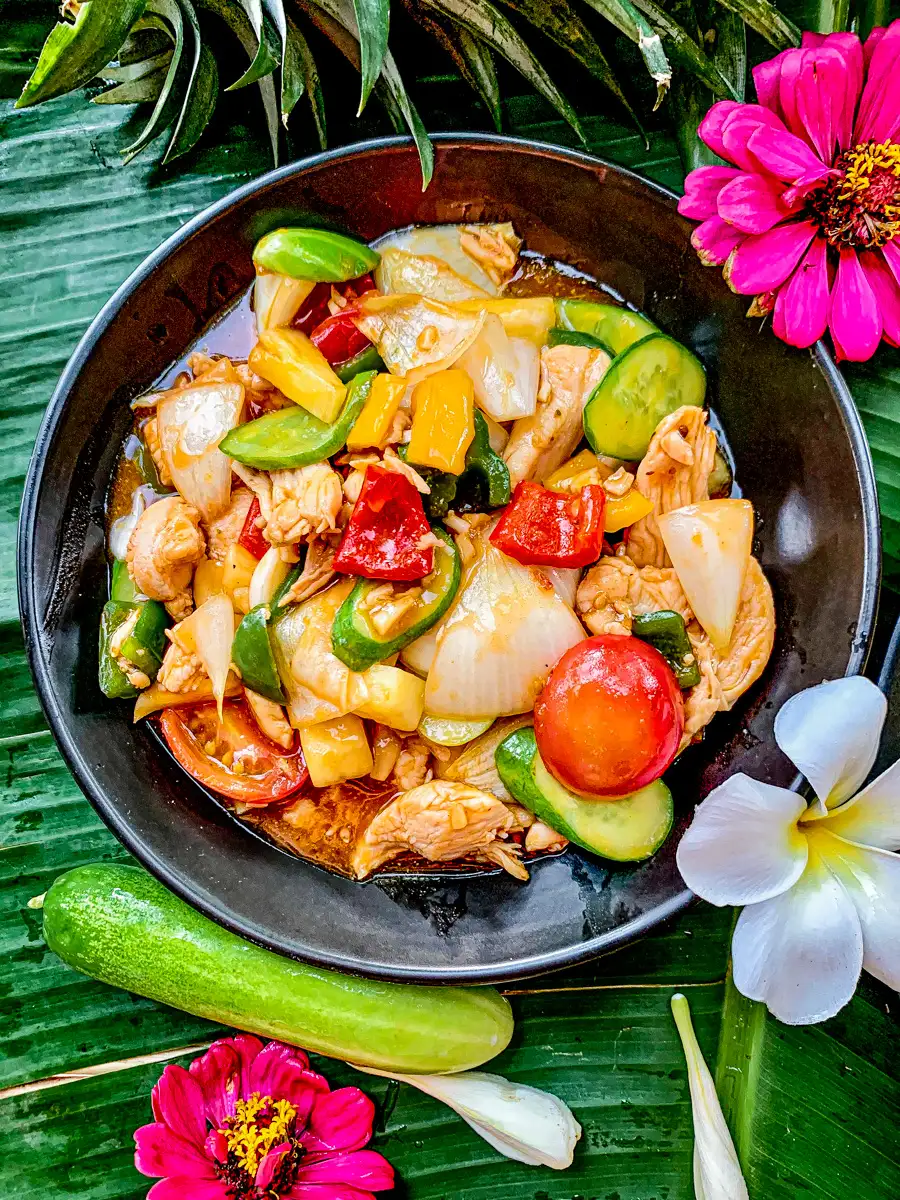 Pad priew wan served in a black bowl with red and yellow bell peppers, cucumber, pineapple, and tomato.
