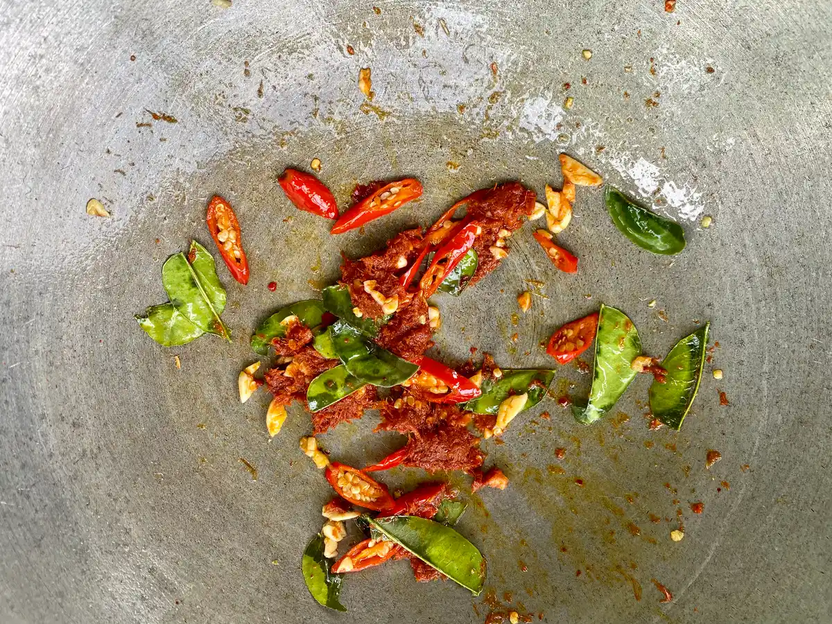 Close-up of sautéed garlic, chilies, and kaffir lime leaves in a pan.