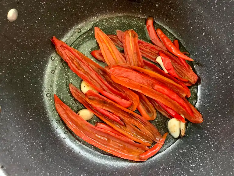 Simmering red chilies and garlic in a saucepan to soften.