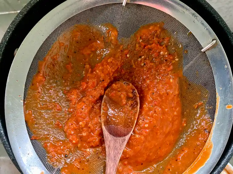 Straining blended chili mixture through a fine mesh sieve.