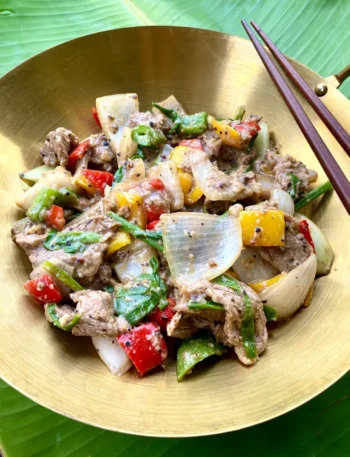 Thai black pepper beef stir-fry with bell peppers, onions, and black pepper sauce in a golden dish.