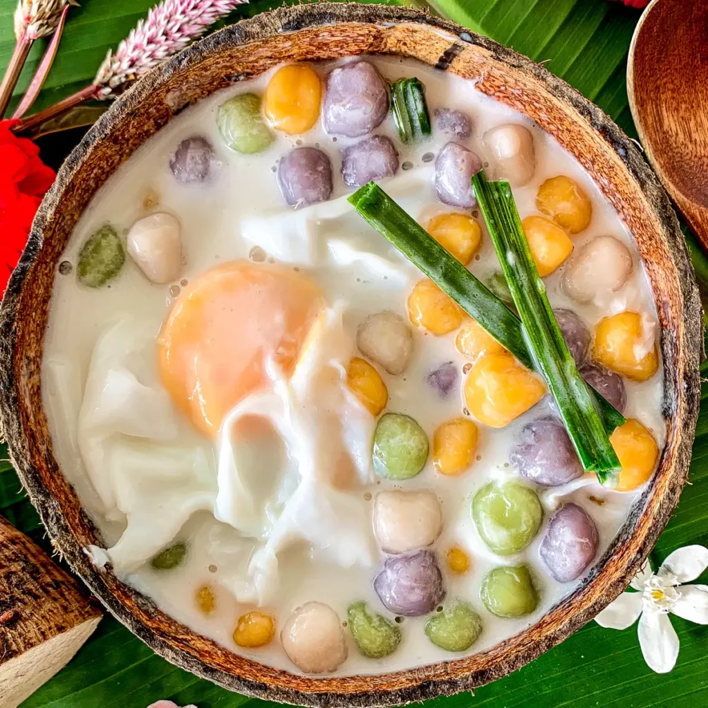 Thai bua loy dessert with poached egg, pandan leaves, and multi-colored rice balls in coconut milk.