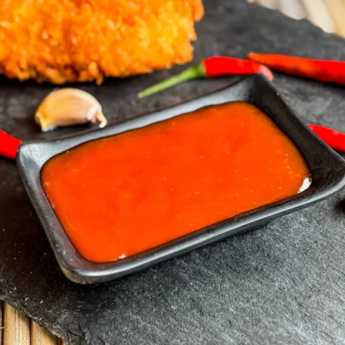 Thai hot sauce in a black dipping bowl with fresh garlic and Thai chili peppers.
