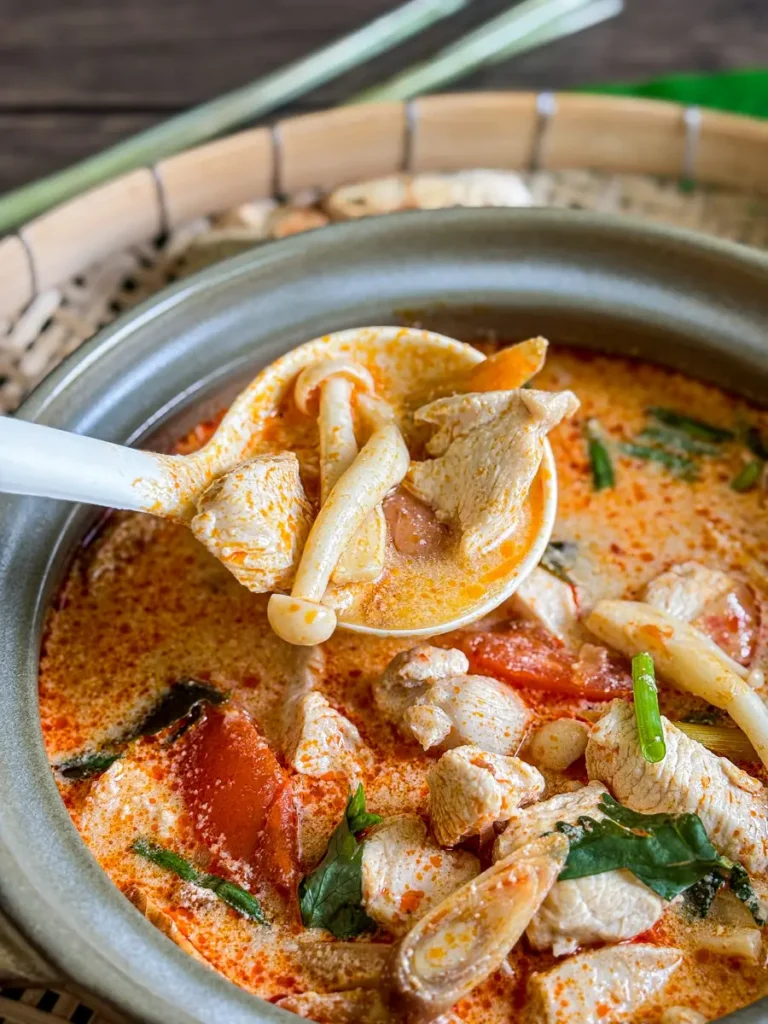 Tom yum chicken soup in a clay bowl with galangal, kaffir lime leaves, and red chili oil.