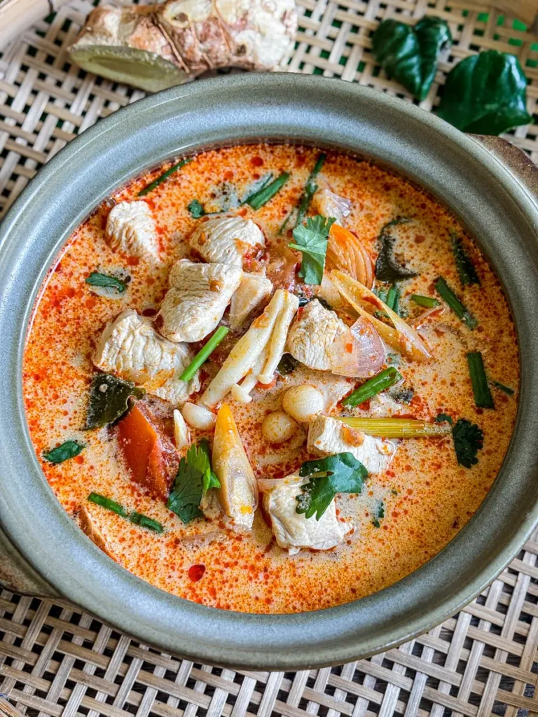 Thai tom yum gai soup with chicken, straw mushrooms, tomatoes, and herbs in a creamy broth.