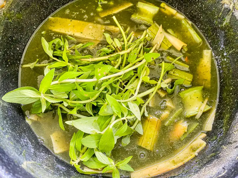 Adding rice paddy herb to finish traditional gang nor mai bamboo soup in a non-stick pot.